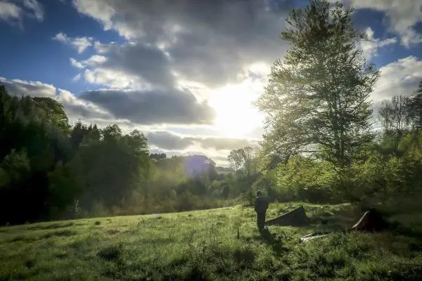 Lichtstrahlen fallen auf eine Wiese mit Zelt und Bäumen im Hintergrund