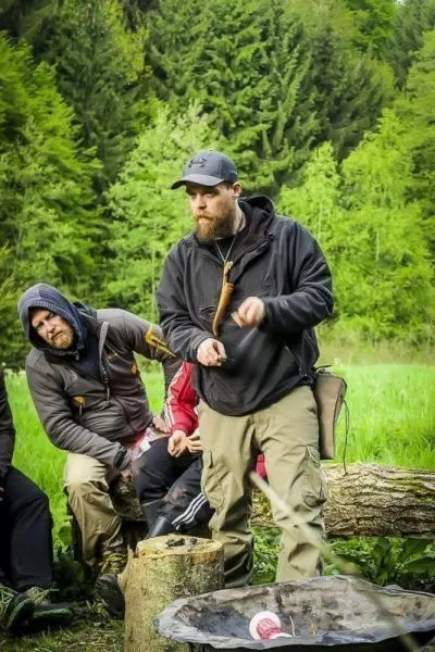 Mann demonstriert Holzarbeit mit einem Messer, Zuschauer beobachten aufmerksam