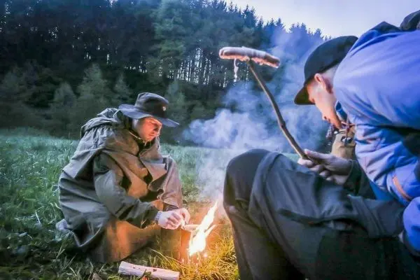Mann entzündet Zunder mit Feuerstahl, während ein anderer zuschaut