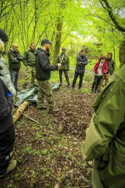 Mann erklärt Techniken im Wald, Teilnehmer hören aufmerksam zu