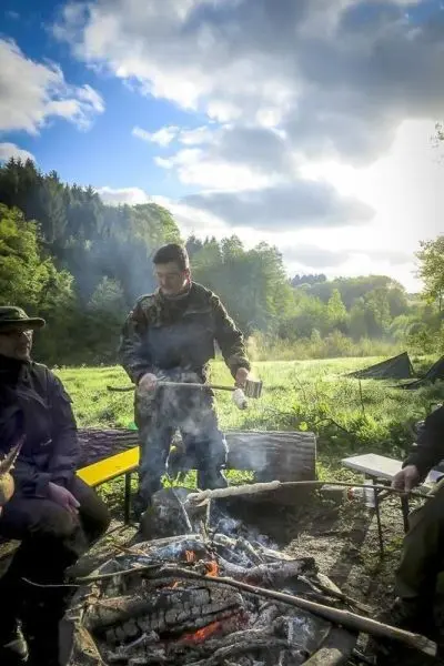 Mann hält einen Stock über ein offenes Feuer in einer Waldumgebung