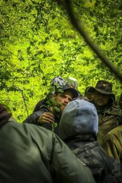 Mann hält einen Zweig in einer Gruppe von Personen im Wald