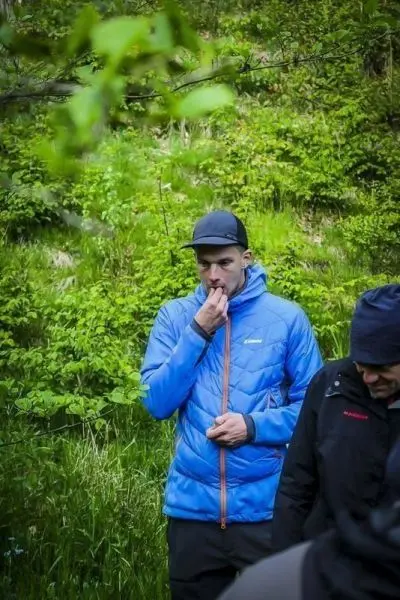 Mann im blauen Jacket steht in der Natur und hält sich die Hand vor den Mund