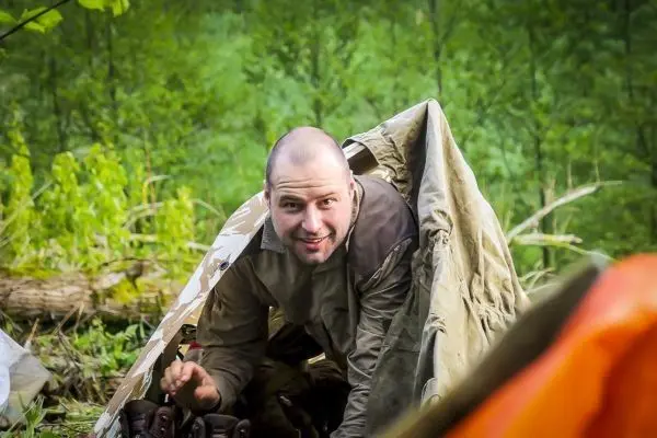 Mann kriecht aus einer Tarp-Notunterkunft in der Natur