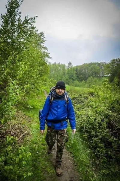 Mann mit Rucksack wandert auf einem schmalen Pfad durch bewaldetes Gelände