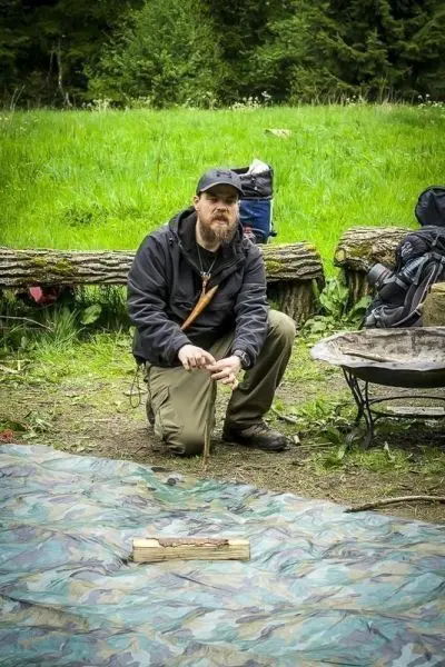 Mann sitzt auf einer Plane und bearbeitet einen Holzstock