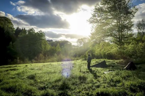 Mann steht in einer Wiese neben einer Tarp-Notunterkunft unter Bäumen
