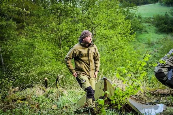 Mann steht neben einer Tarp-Notunterkunft in bewaldeter Umgebung