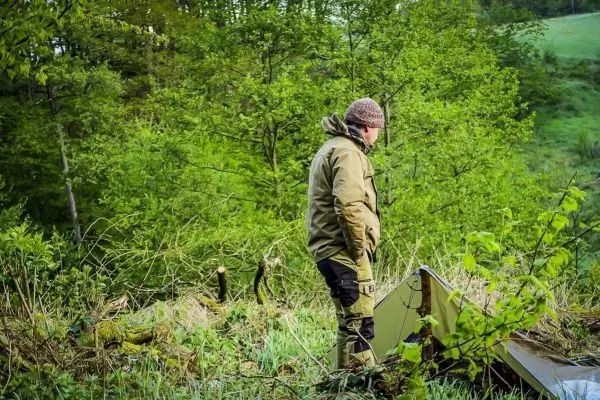 Mann steht neben einer Tarp-Notunterkunft in bewaldeter Umgebung