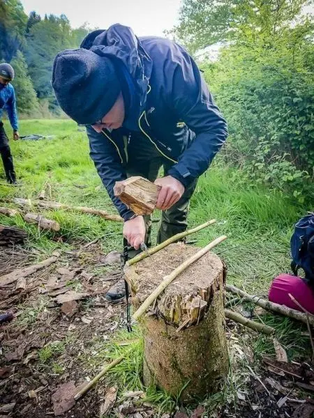 Person bearbeitet Holzstück auf einem Baumstumpf beim Überlebenstraining