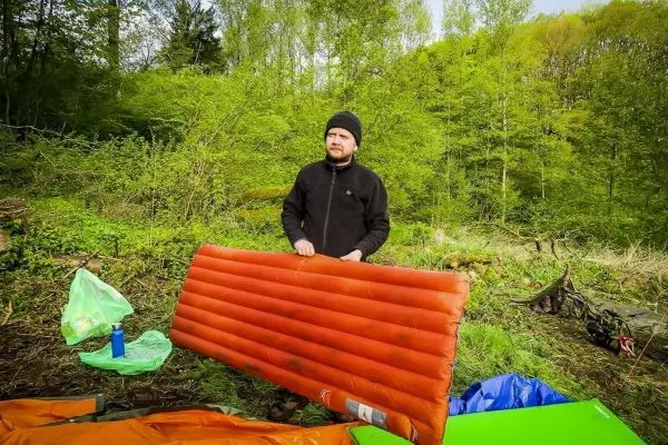 Person hält eine orangefarbene Isomatte in einem grünen Wald