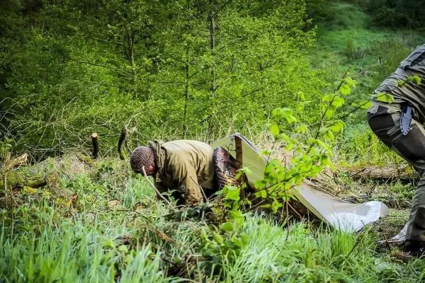 Person kriecht unter einer Tarp-Notunterkunft in bewaldeter Umgebung