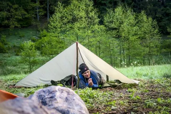 Person sitzt in einer Tarp-Notunterkunft und hält die Hände zusammen