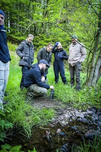 Person untersucht Wasserquelle, während andere zuschauen beim Überlebenstraining