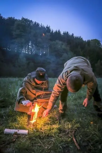 Person zündet Feuer an, während andere Person zuschaut beim Survival Training