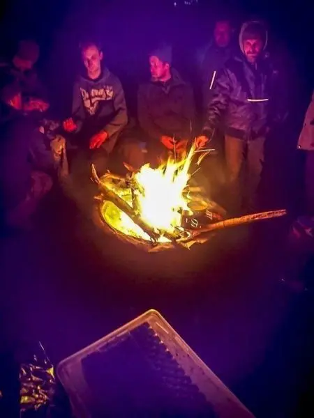 Personen sitzen um ein Feuer und unterhalten sich beim Überlebenstraining