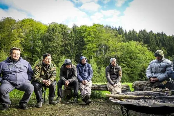 Sechs Personen sitzen auf Baumstämmen um ein kleines Lagerfeuer