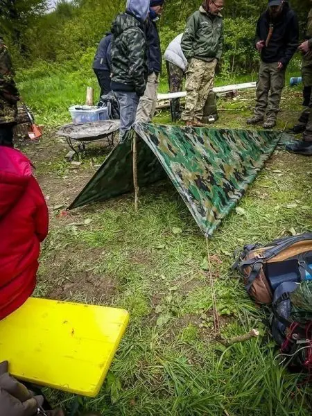Tarp-Notunterkunft aus Tarnmaterial mit improvisierten Stangen auf dem Boden