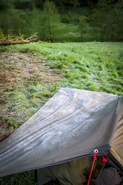 Tarp-Notunterkunft mit Frost auf der Oberfläche in einer grünen Wiese