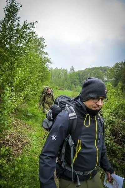 Wanderer mit Rucksack auf schmalem Pfad durch bewaldetes Gebiet