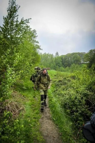 Wanderer mit Rucksack geht auf schmalem Pfad durch bewaldetes Gelände