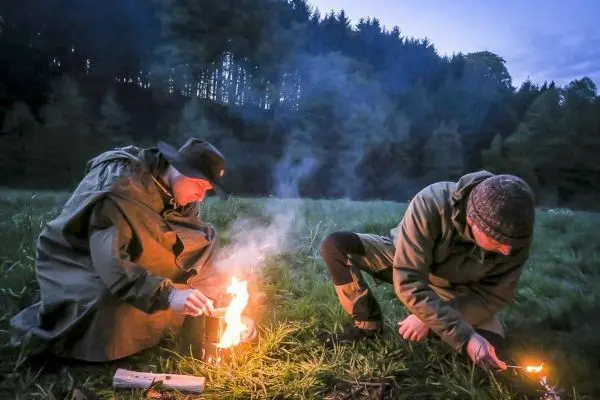 Zunder glimmt in der Nähe von zwei Personen, die Feuer entzünden