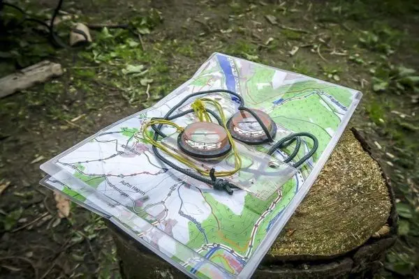 Zwei Kompasse liegen auf einer Landkarte, die auf einem Baumstumpf platziert ist