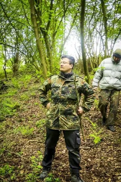 Zwei Personen im Wald, eine hält einen Stock und schaut nachdenklich