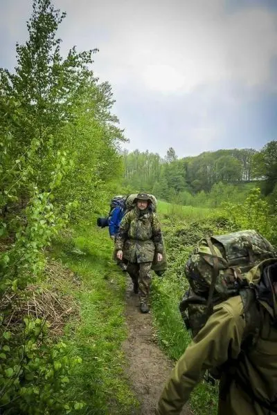 Zwei Personen mit Rucksäcken gehen einen schmalen Weg entlang, umgeben von Bäumen