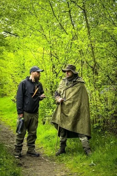 Zwei Personen stehen auf einem Weg zwischen Bäumen und unterhalten sich