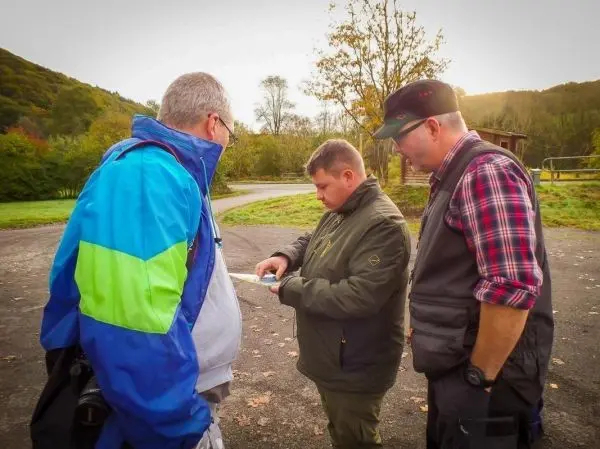 Drei Personen betrachten eine Karte auf einem Parkplatz in der Natur