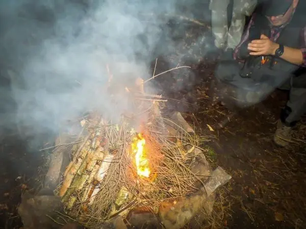 Feuer brennt in einem Steinkreis, Person sitzt daneben