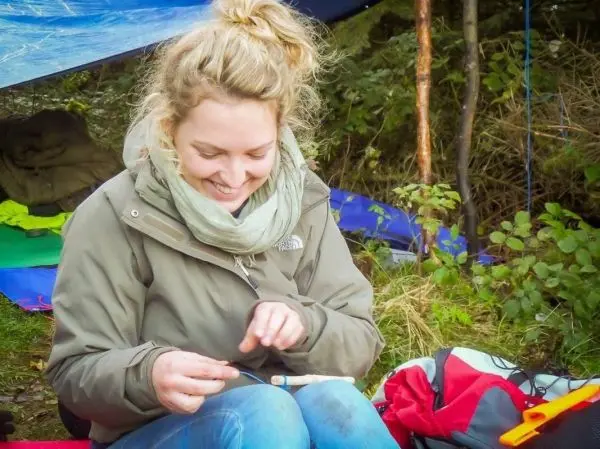 Frau schnitzt mit einem Messer an einem Holzstück unter einem Tarp