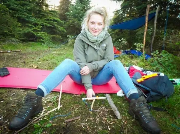 Frau sitzt auf einer Matte und bearbeitet Holzstücke mit einem Messer