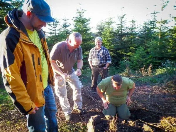 Gruppierung von vier Personen um eine kleine Feuerstelle im Wald, einer kniet vor der Feuerstelle