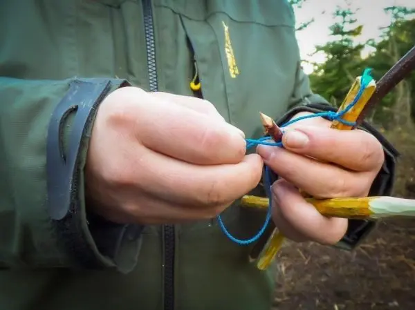 Hände binden eine Schnur um einen Holzstock zur Konstruktion