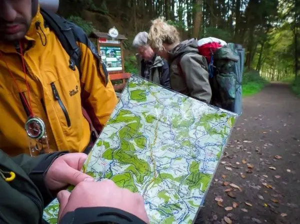 Händedruck hält eine Karte, während zwei Personen im Hintergrund stehen