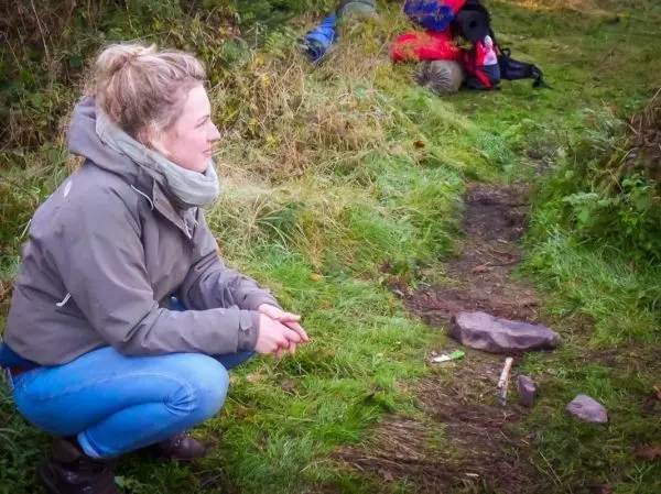 Kniende Person beobachtet den Bodenweg mit Steinen und Holzstücken