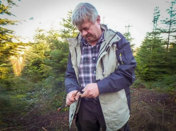 Mann bearbeitet ein Werkzeug in einem Waldgebiet zwischen Nadelbäumen