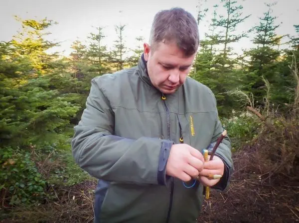 Mann bearbeitet einen Stock mit einem Messer im Wald