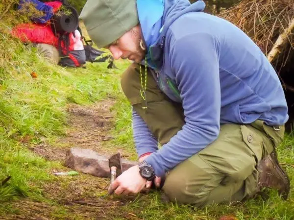 Mann bearbeitet Holzstück mit einem Messer auf dem Boden
