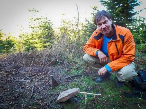 Mann kniet neben einem großen Stein und Holzstücken im Wald
