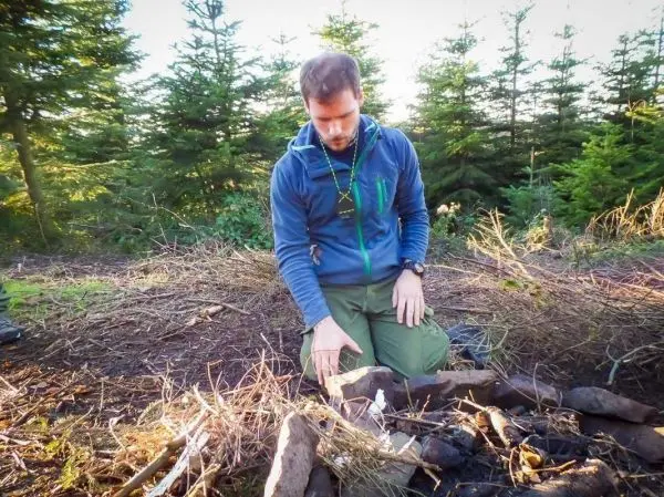 Mann kniet neben einem kleinen Feuerplatz mit Holz und Zunder
