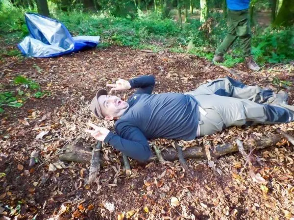 Mann liegt auf einer improvisierten Liege aus Ästen im Wald