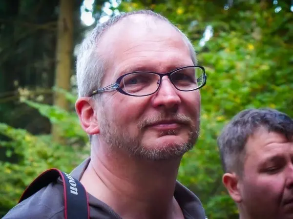 Mann mit Brille und Kamera im Wald, unscharfer Hintergrund