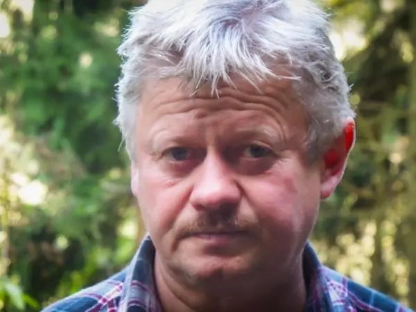 Mann mit grauen Haaren und kariertem Hemd vor grüner Hintergrundvegetation