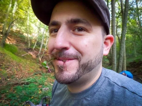 Mann mit Zweigen im Mund lächelt in einem Waldgebiet