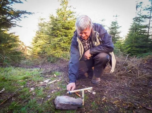 Mann positioniert einen Stock auf einem Stein zur Konstruktion einer Schlagfalle