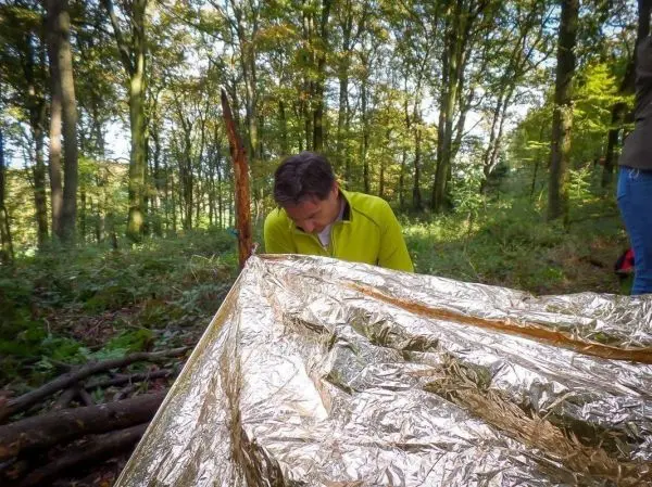 Mann richtet Tarp-Notunterkunft aus reflektierendem Material im Wald ein