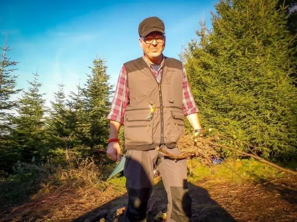 Mann trägt Äste und steht auf einem Waldweg zwischen Nadelbäumen